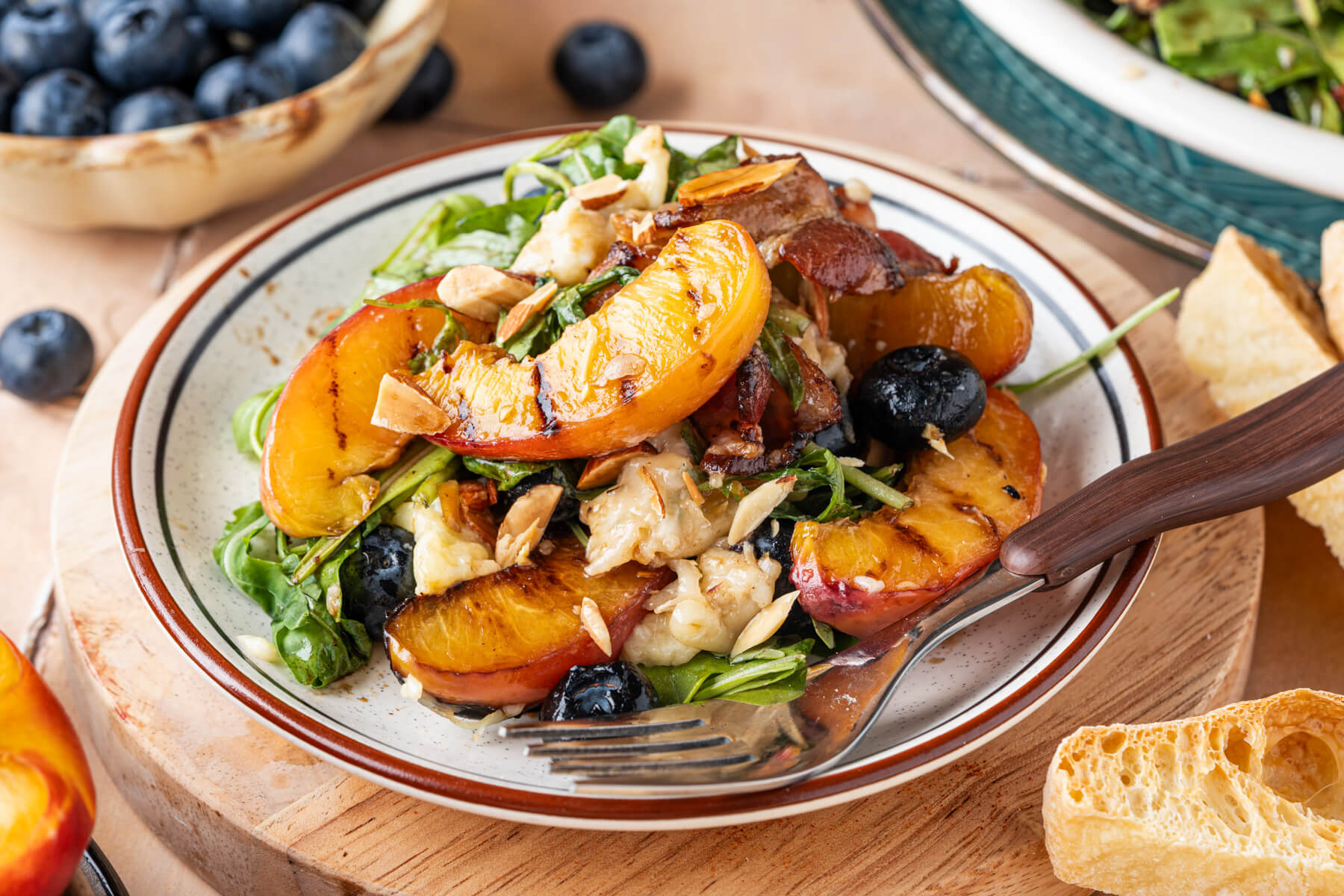 A salad plate containing grilled peaches, green arugula, blueberries, toasted almonds, and torn burrata.