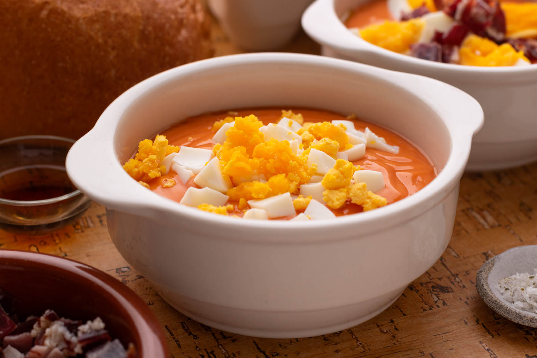 A white soup bowl filled with vibrant orange Salmorejo garished with diced eggs.