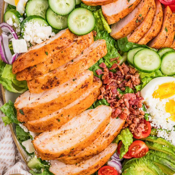 Close up photo of sliced smoked chicken breast on top of an arranged cobb salad.