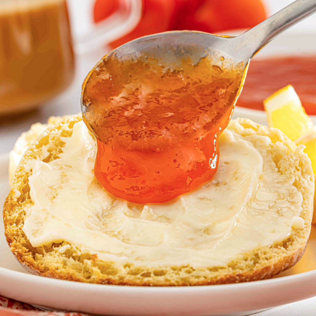 Apricot jam dripping from a spoon onto a buttered English muffin.