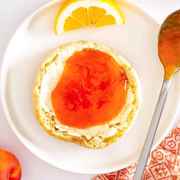 Apricot jam slathered onto a buttered English muffin on a white plate.