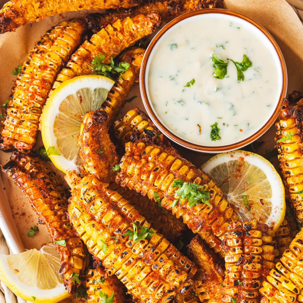 Close up photo of spiced and caramelized corn ribs with a small bowl of creamy dip and lemon wedges.