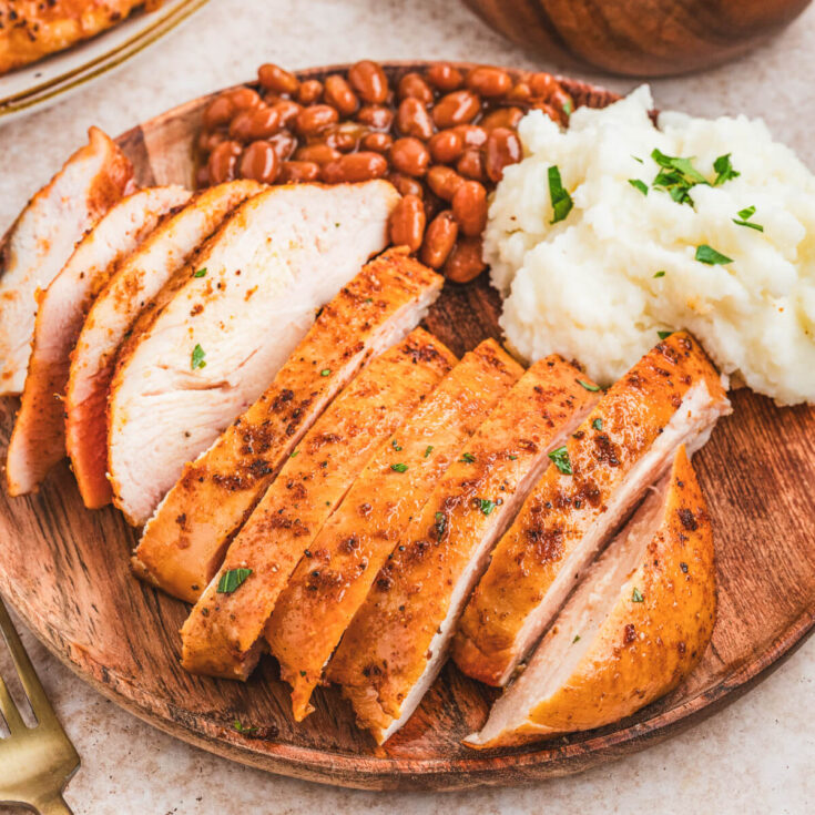 A sliced chicken breast on a plate beside baked beans and mashed potatoes.