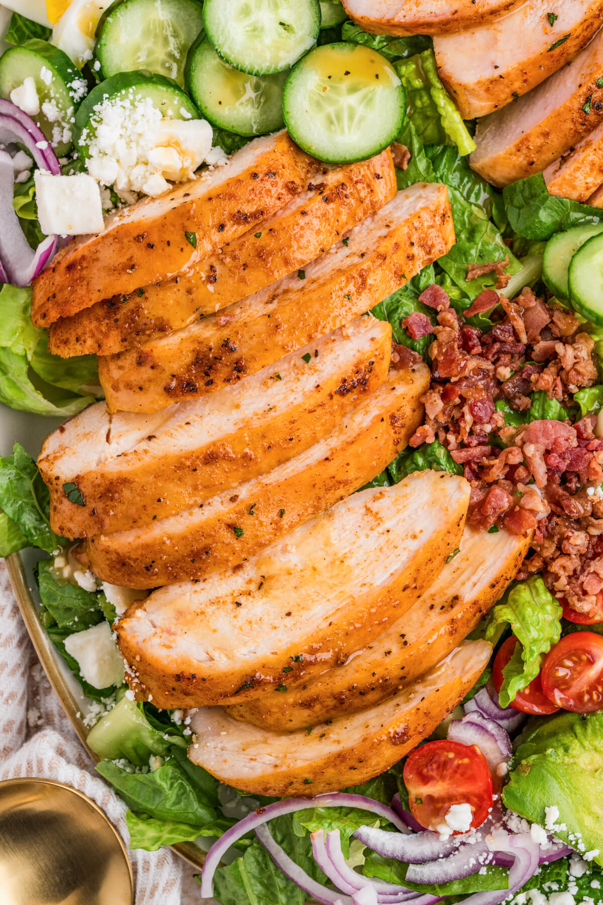 Close up photo of sliced smoked chicken breast on top of an arranged cobb salad.