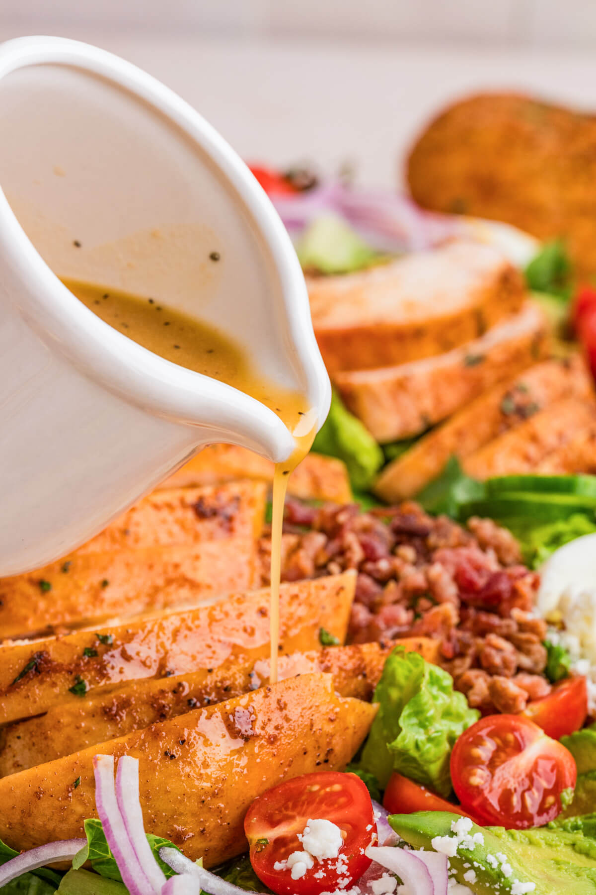 A small white pitcher pouring salad dressing over a platter of chicken cobb salad.