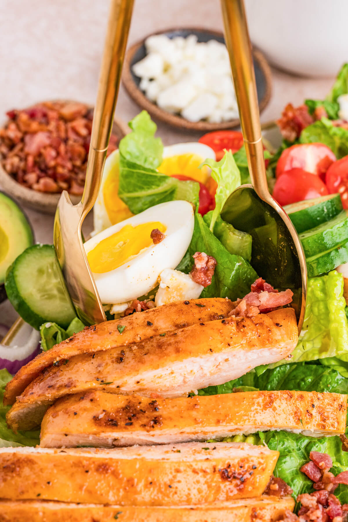 A pair of salad servers grabbing a serving of chicken cobb salad from a large salad platter.