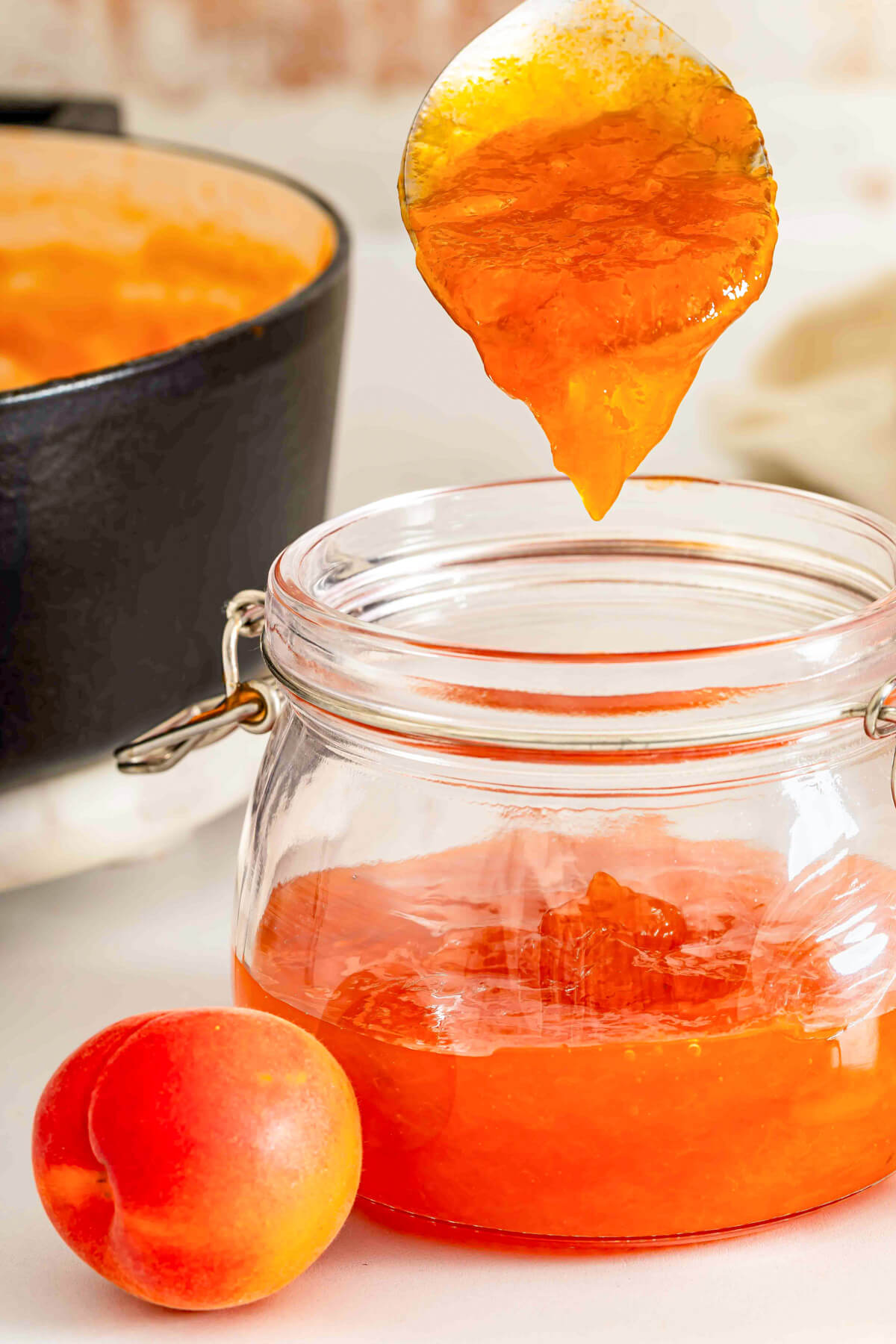 Apricot jam dripping from a spoon into a jar of the same jam.