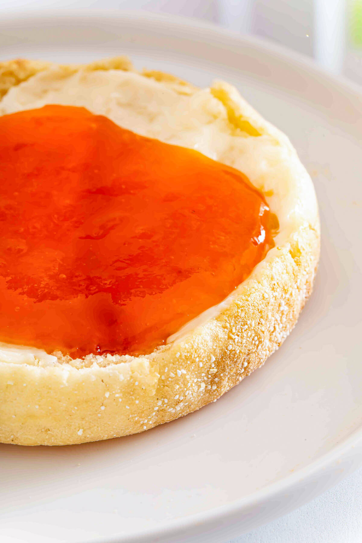Apricot jam slathered onto a buttered English muffin on a white plate.