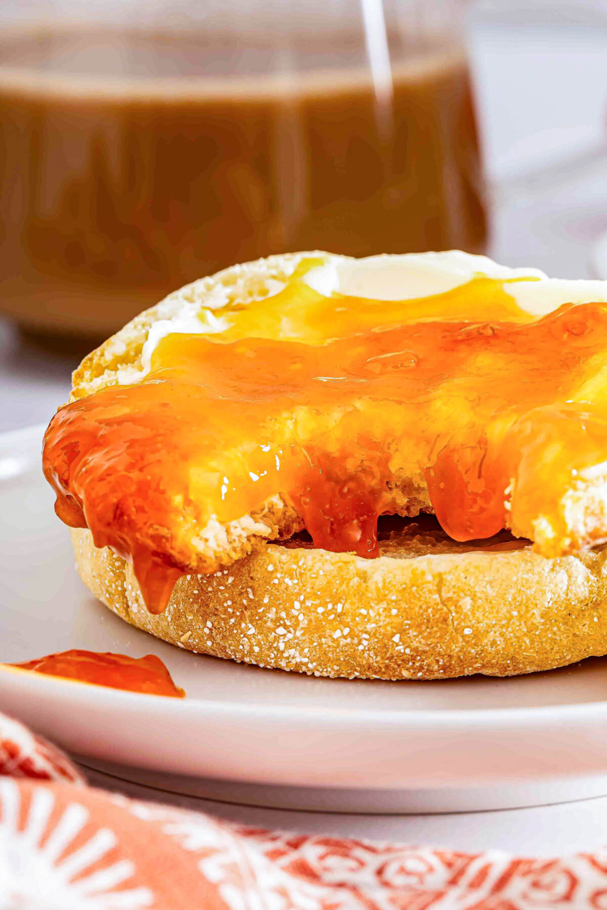 Apricot jam slathered onto a buttered English muffin with a bite missing on a white plate.