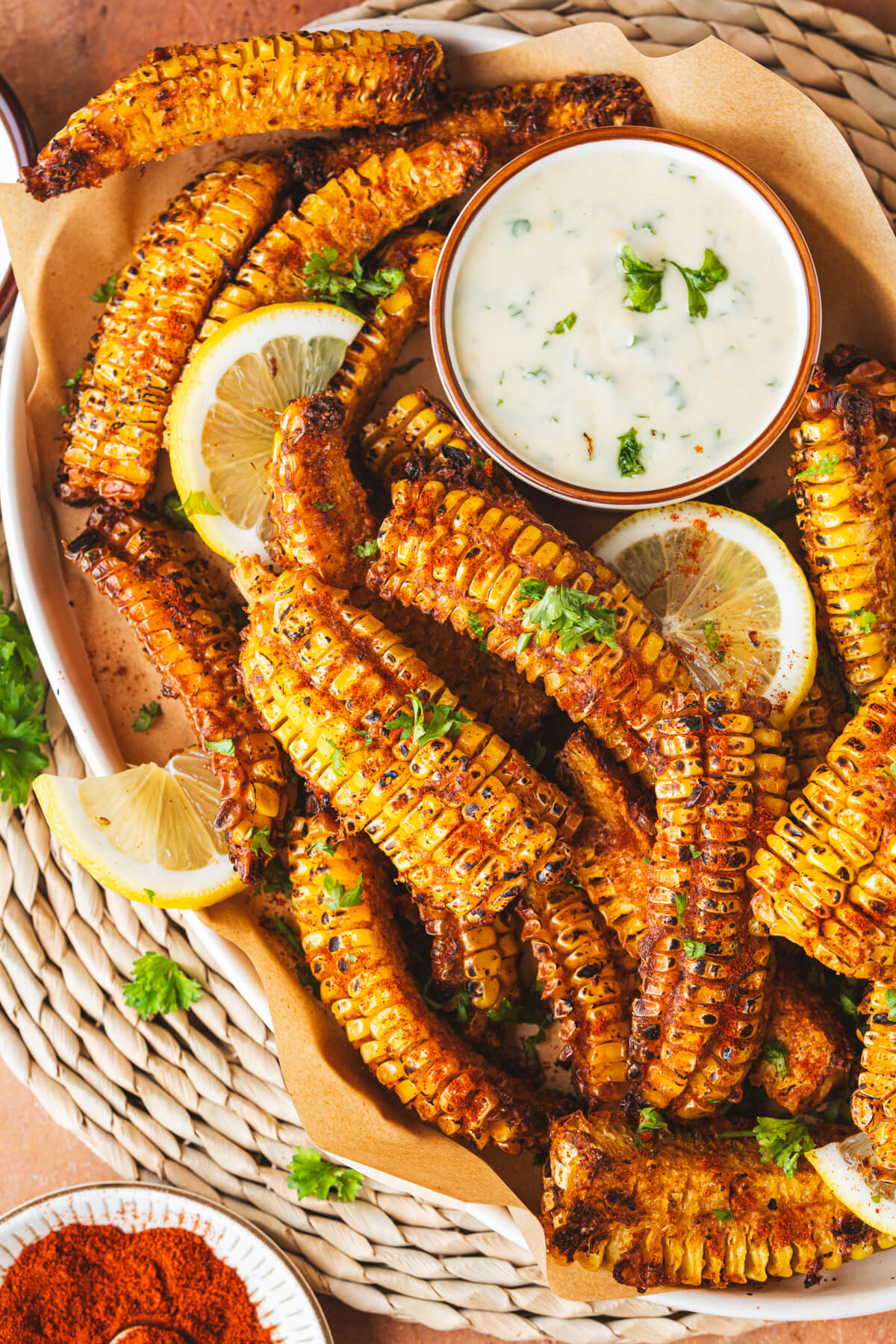 A platter of spiced and caramelized corn ribs with a small bowl of creamy dip and lemon wedges.