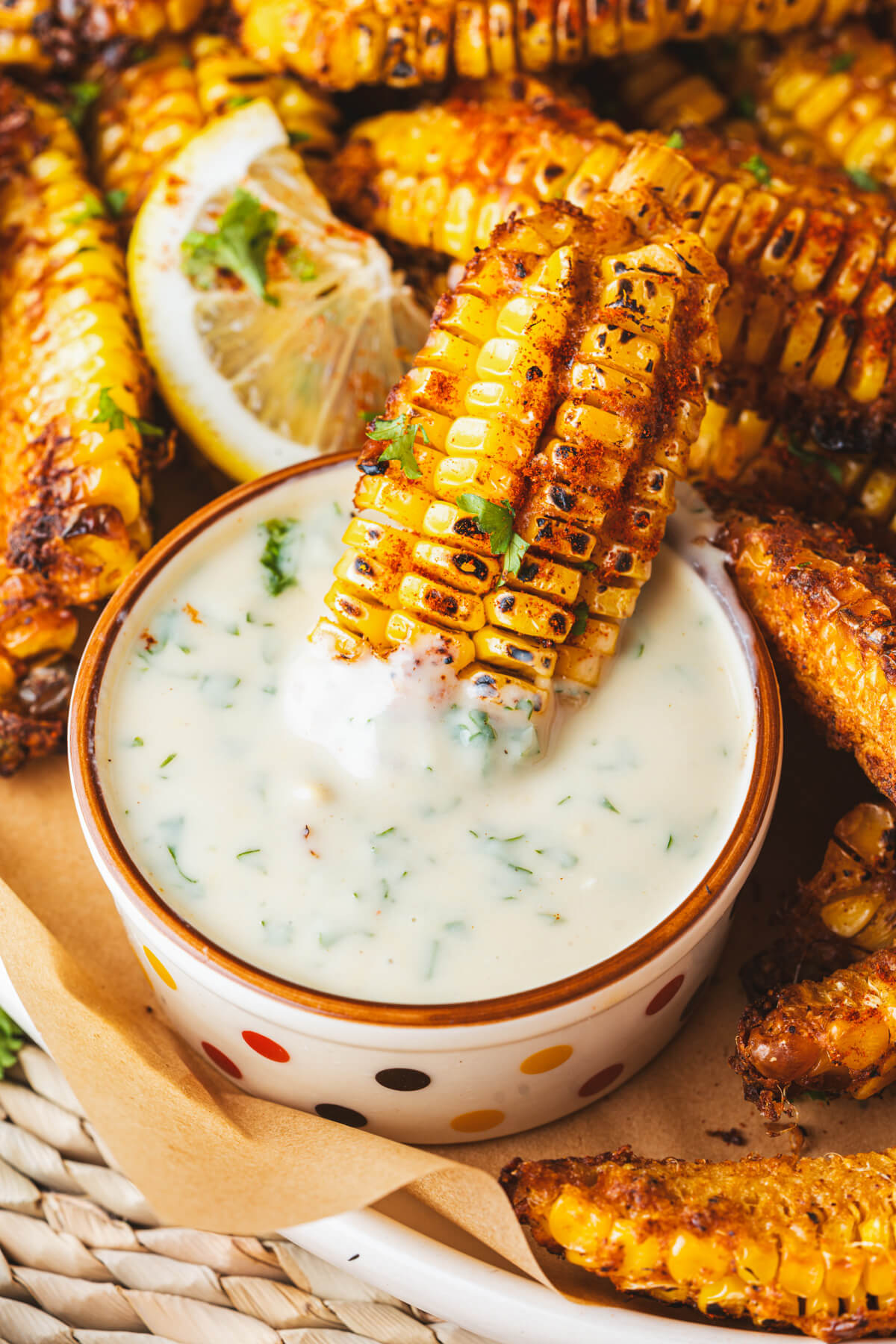 A spicy caramelized corn rib sits in a small bowl of creamy dip.