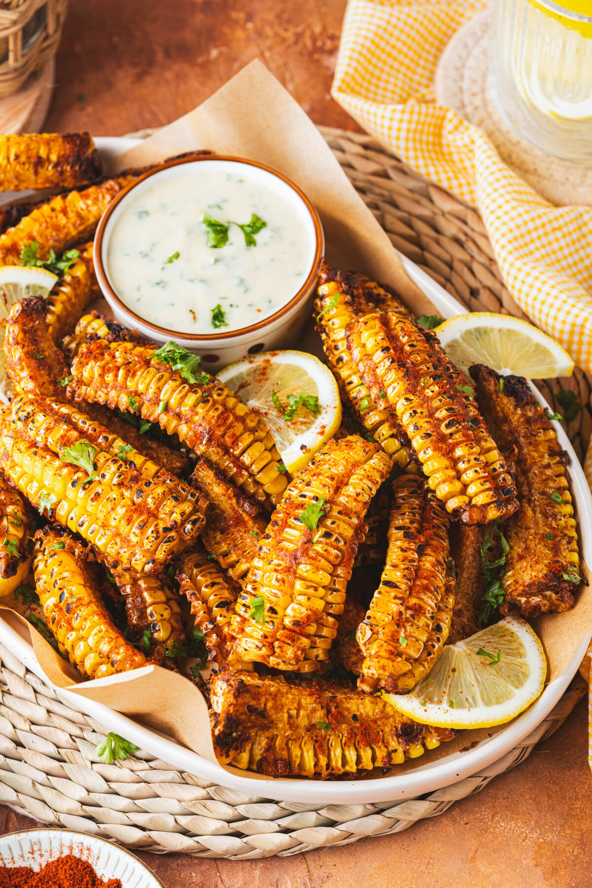 A platter of spiced and caramelized corn ribs with a small bowl of creamy dip and lemon wedges.