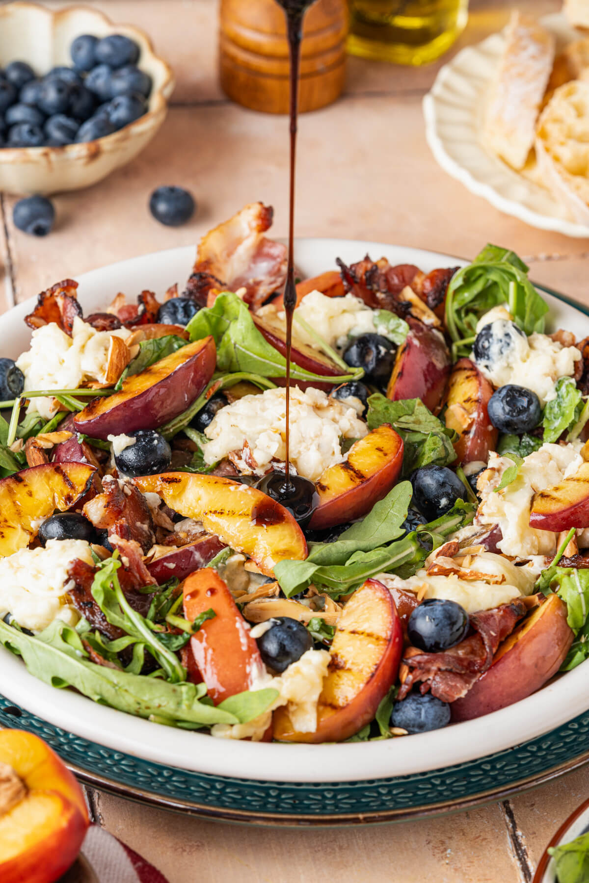 Balsamic salad dressing being poured over a grilled peach burrata salad.