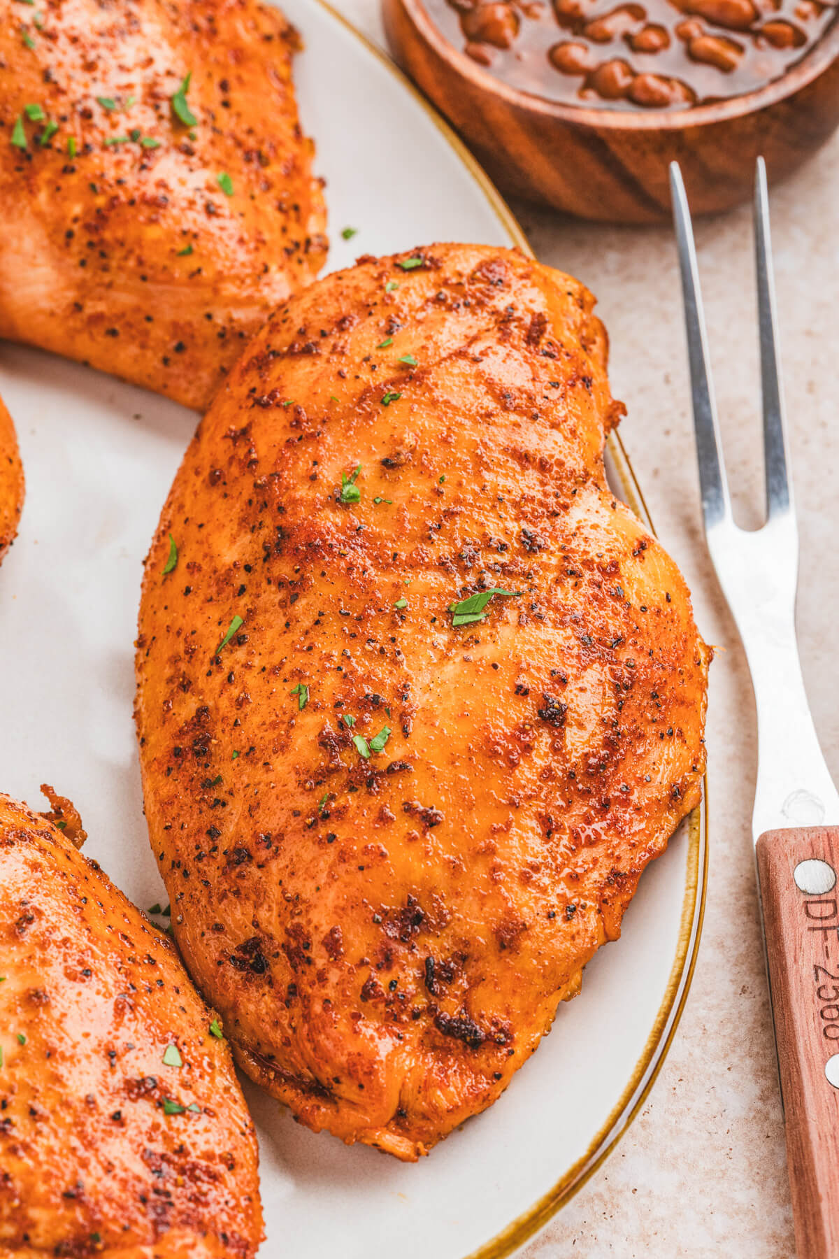 A whole smoked chicken breast on a plate beside a wooden handled fork.