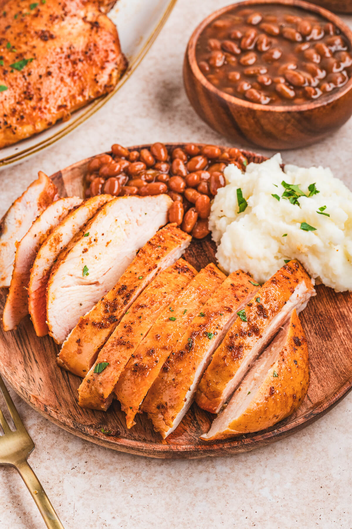 A sliced chicken breast on a plate beside baked beans and mashed potatoes.