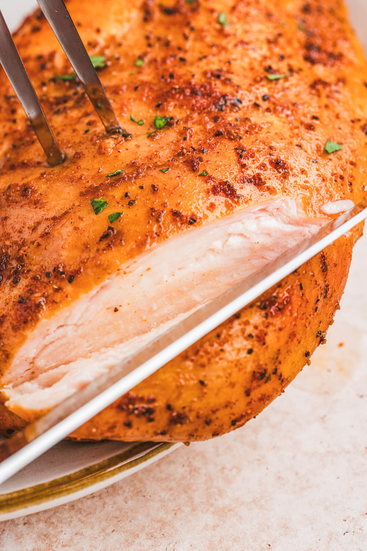 A knife slicing into a juicy smoked chicken breast.