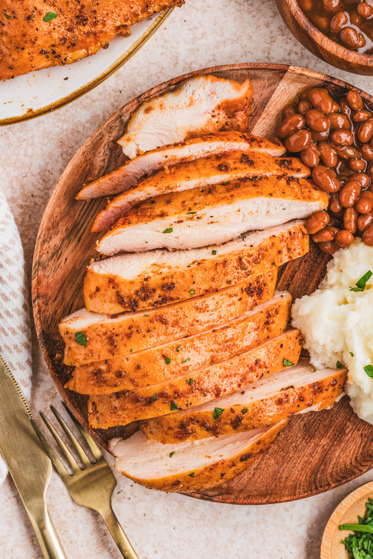 A sliced chicken breast on a plate beside baked beans and mashed potatoes.