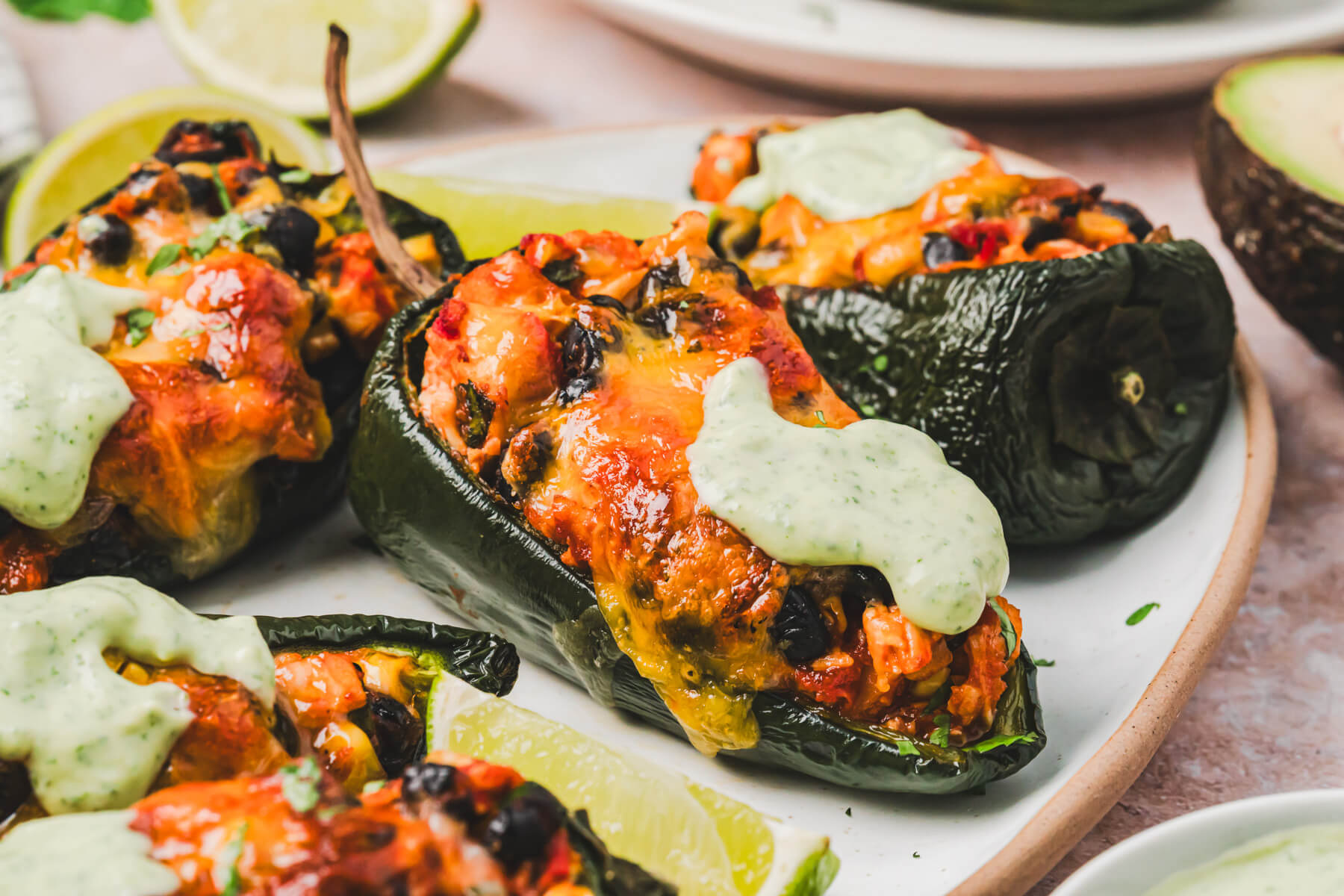 A trio of stuffed poblano peppers topped with a layer of melted cheese and a dollop of cilantro crema on a plate.