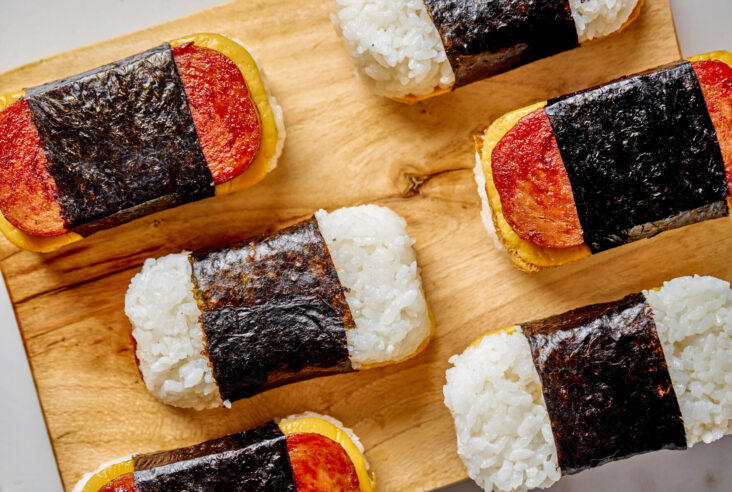 Spam and Egg Musubi wrapped in nori strips on a wooden serving board.