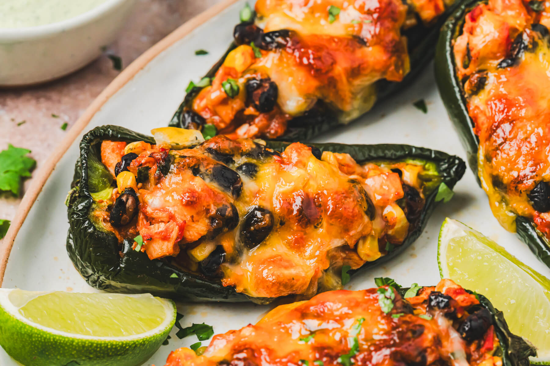 A group of stuffed poblano peppers topped with a layer of melted cheese and a dollop of cilantro crema on a plate.
