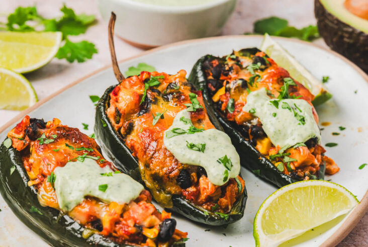 Three stuffed poblano peppers topped with a layer of melted cheese and a dollop of cilantro crema on a plate.
