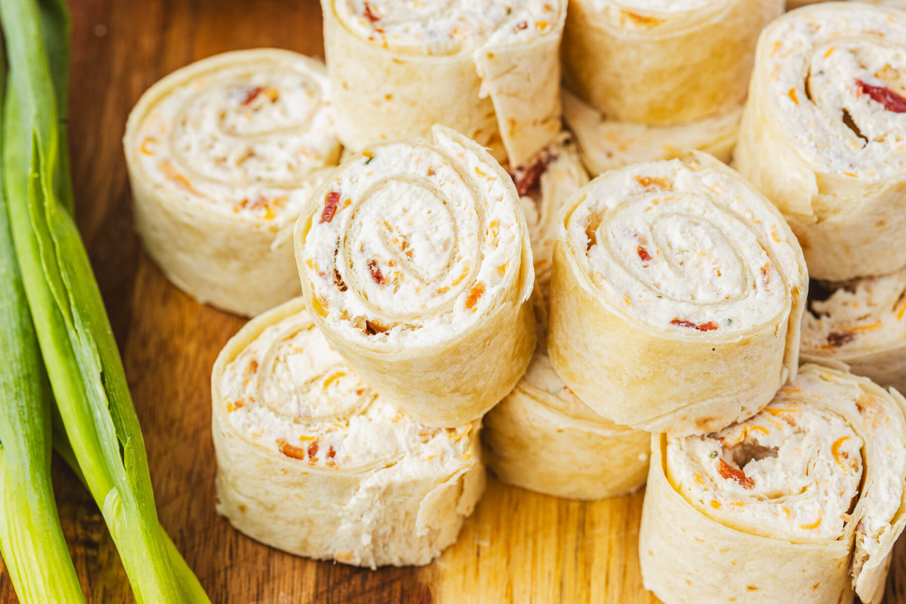 A pile of tortilla pinwheels filled with cream cheese mixture containing bacon, cheddar cheese, and shredded chicken.