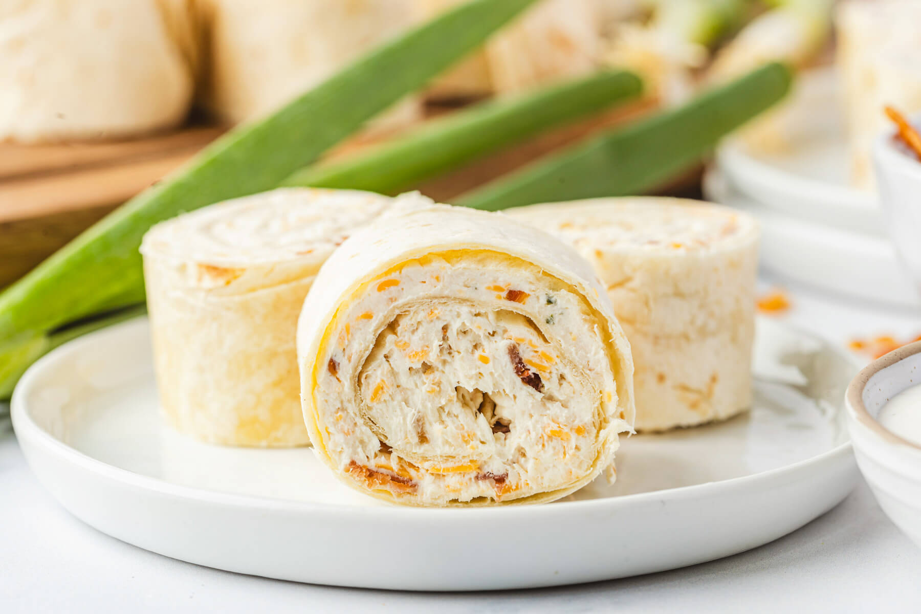 A white plate containing three tortilla pinwheels filled with cream cheese mixture containing bacon, cheddar cheese, and shredded chicken.