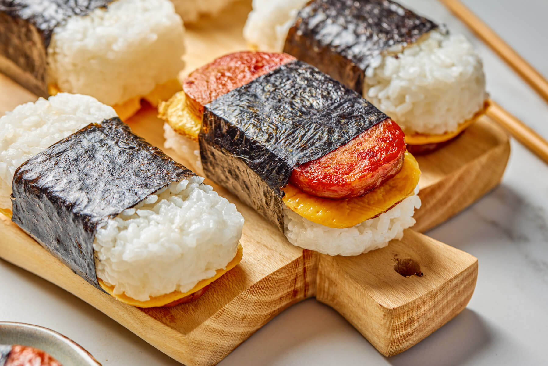 Three Spam and Egg Musubi wrapped in nori strips on a wooden serving board.