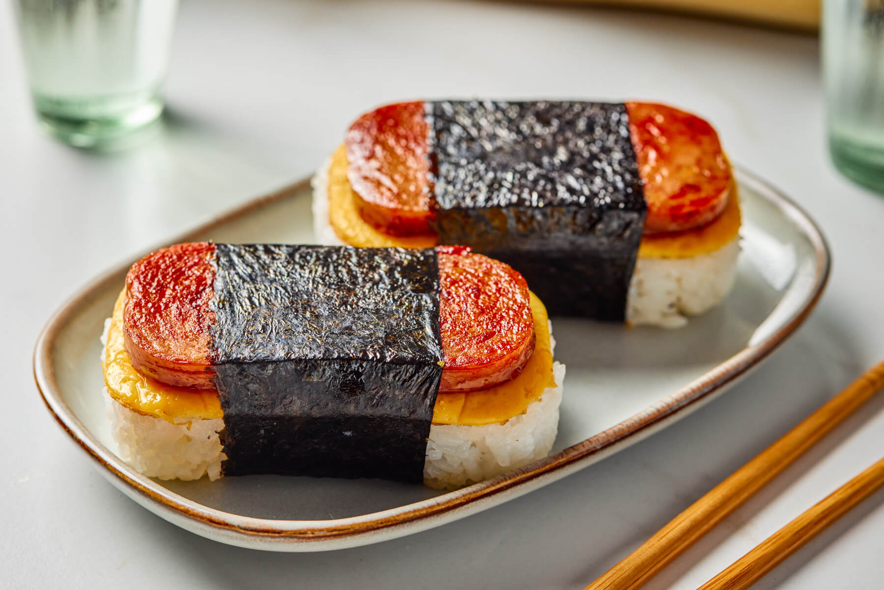 Two Spam and Egg Musubi wrapped in nori strips on an oval plate.