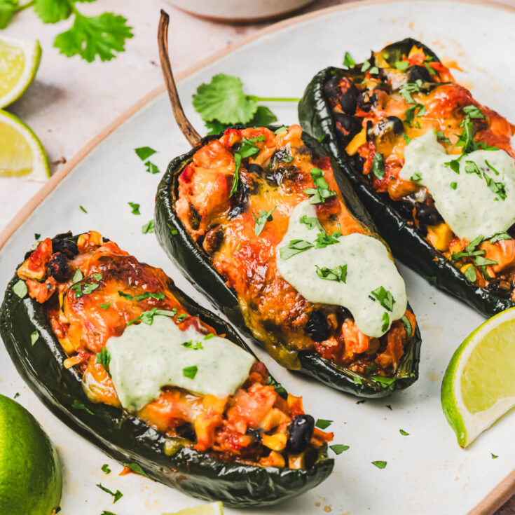 A trio of stuffed poblano peppers topped with a layer of melted cheese and a dollop of cilantro crema on a plate.