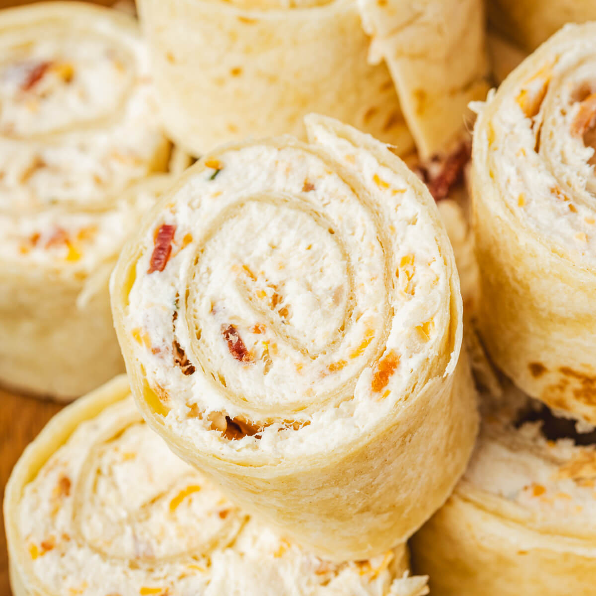 A pile of tortilla pinwheels filled with cream cheese mixture containing bacon, cheddar cheese, and shredded chicken.
