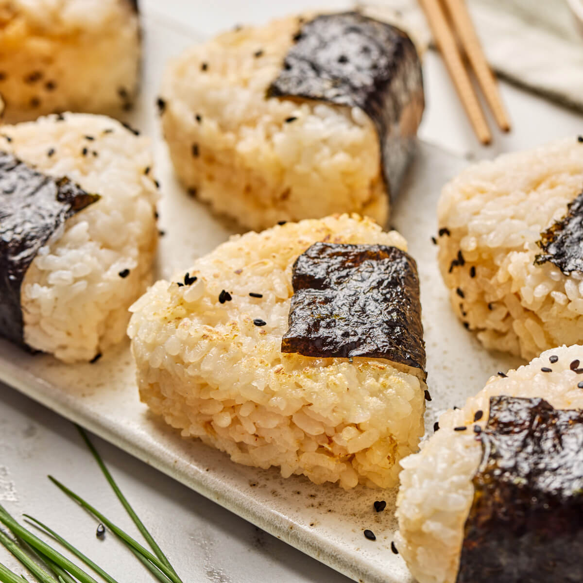 A tray of seasoned Japanese Onigiri wrapped in nori and garnished with black sesame seeds.