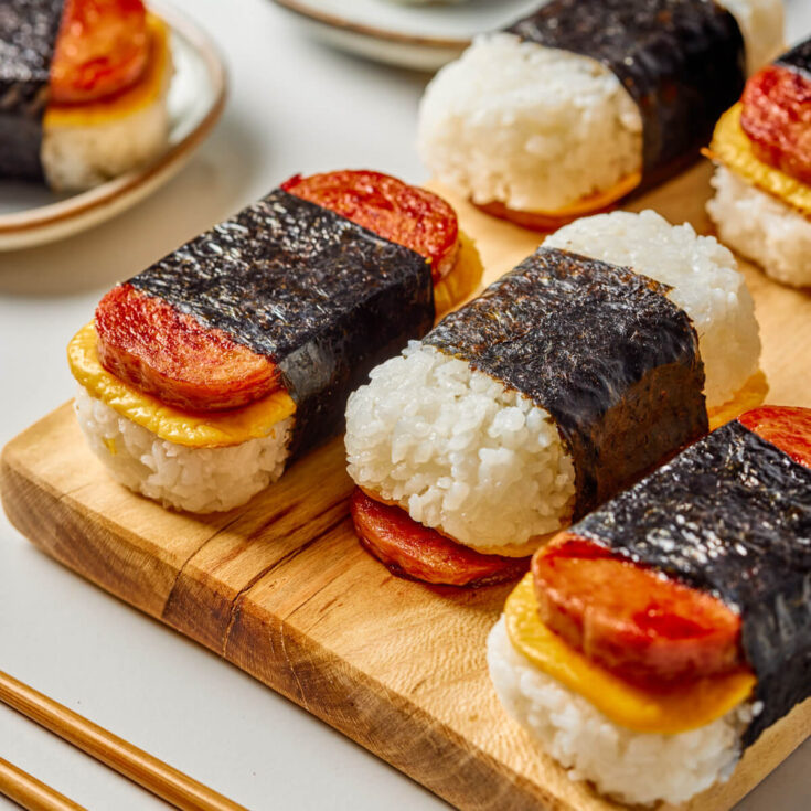 Three Spam and Egg Musubi wrapped in nori strips on a wooden serving board.