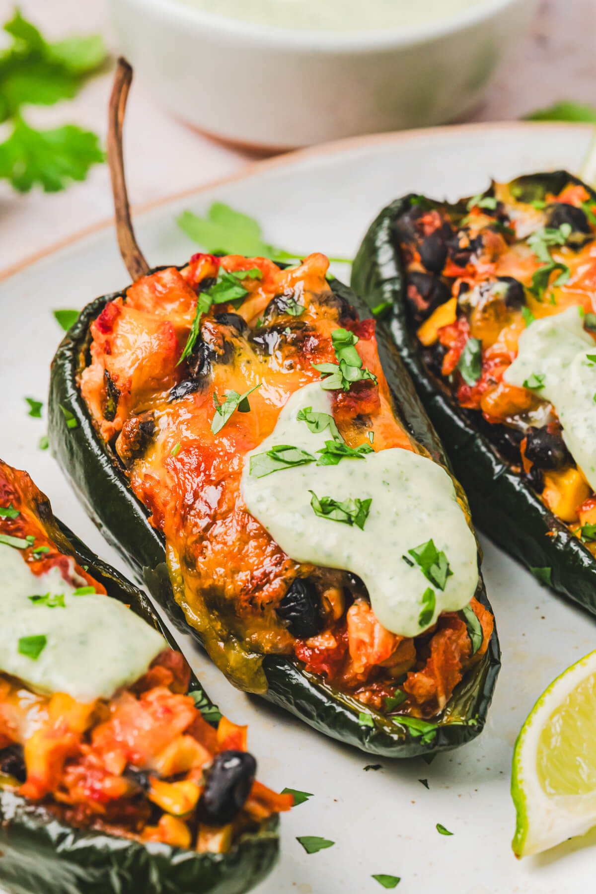 Close up of a stuffed poblano pepper topped with a layer of melted cheese and a dollop of cilantro crema on a plate.