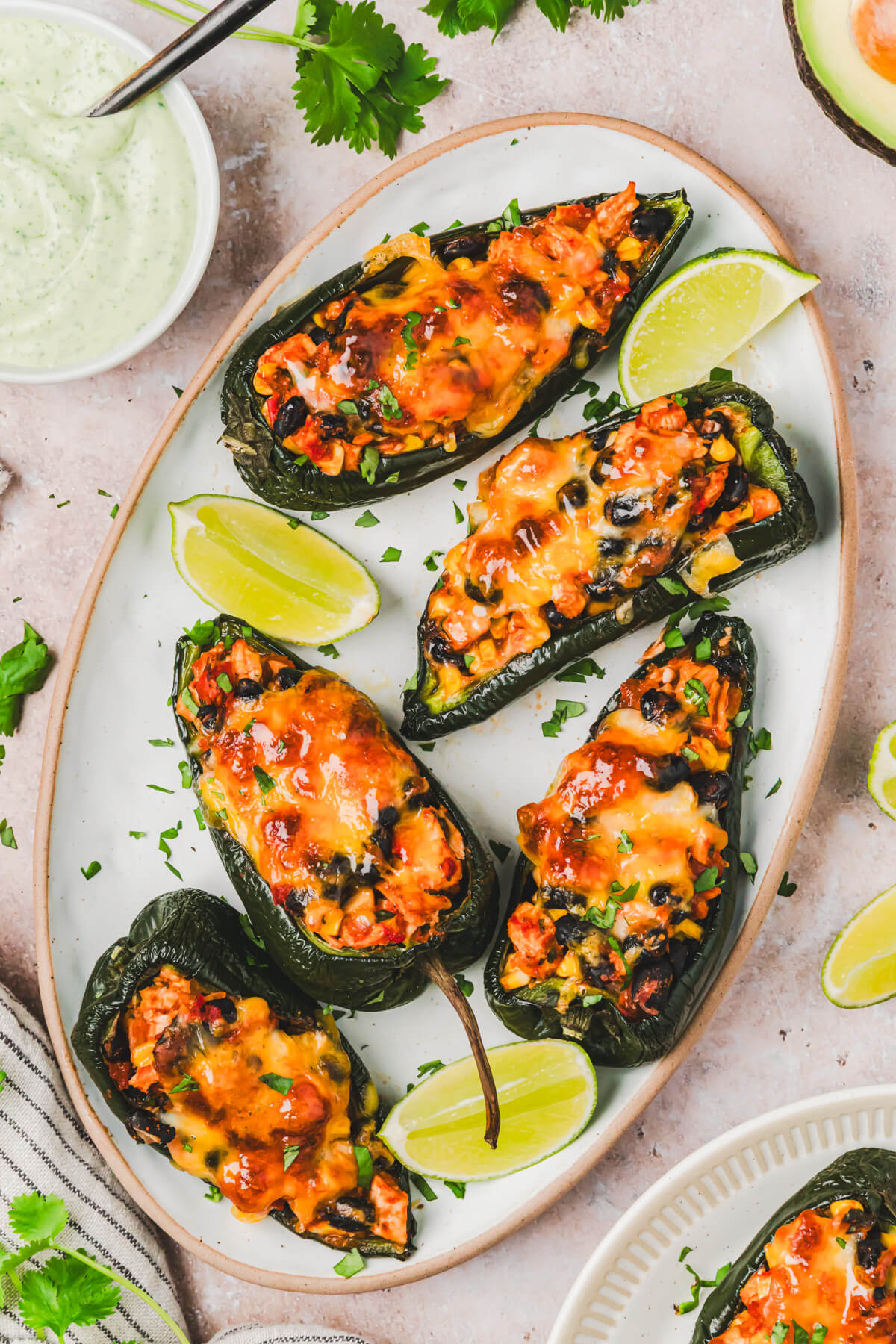 Five stuffed poblano peppers topped with a layer of melted cheese and a dollop of cilantro crema on a plate.