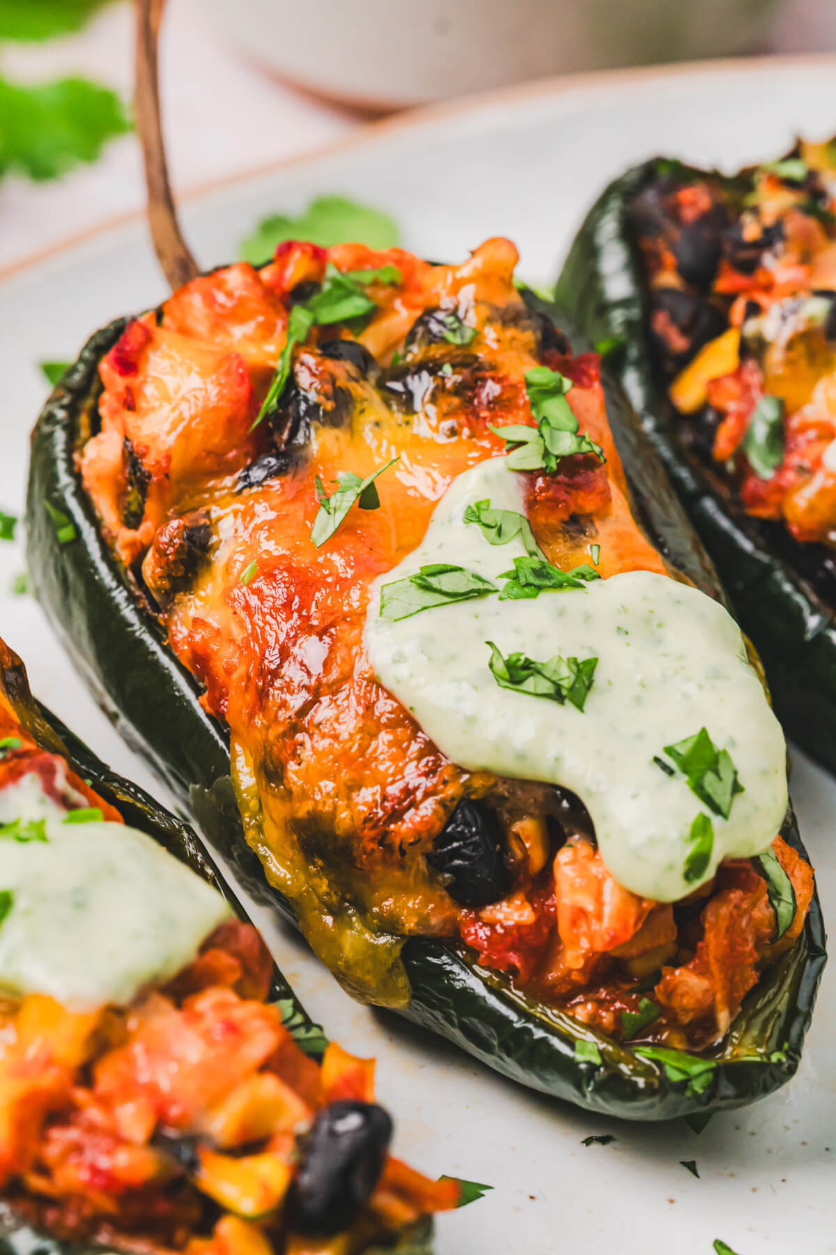 Close up of a stuffed poblano pepper topped with a layer of melted cheese and a dollop of cilantro crema on a plate.