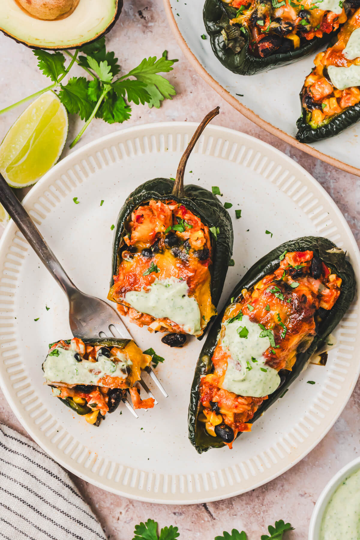 A plate containing two cheesy stuffed poblano peppers with a fork stealing a bite from one pepper.