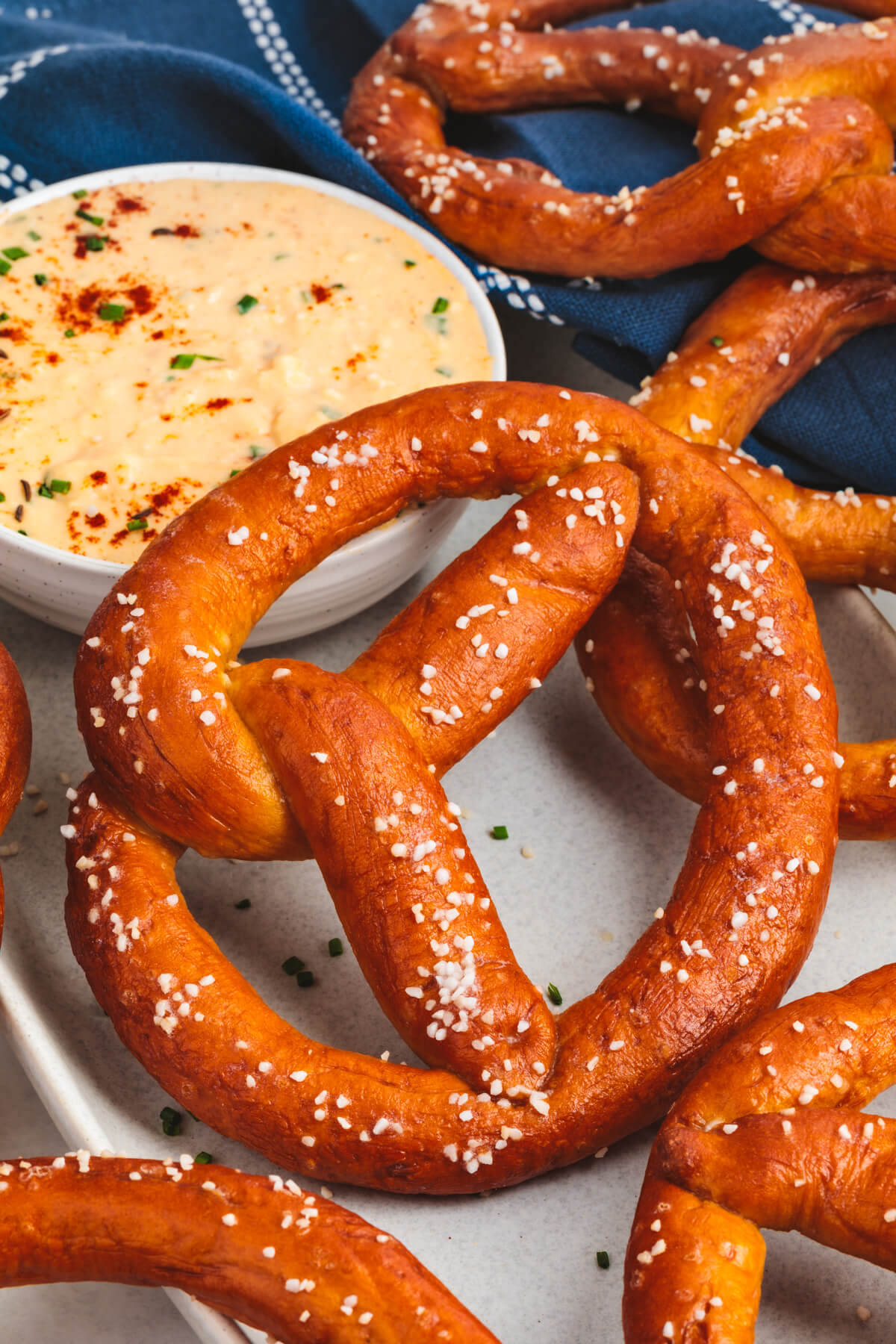 A group of deep brown homemade pretzels in front of a bowl of Obatzda.