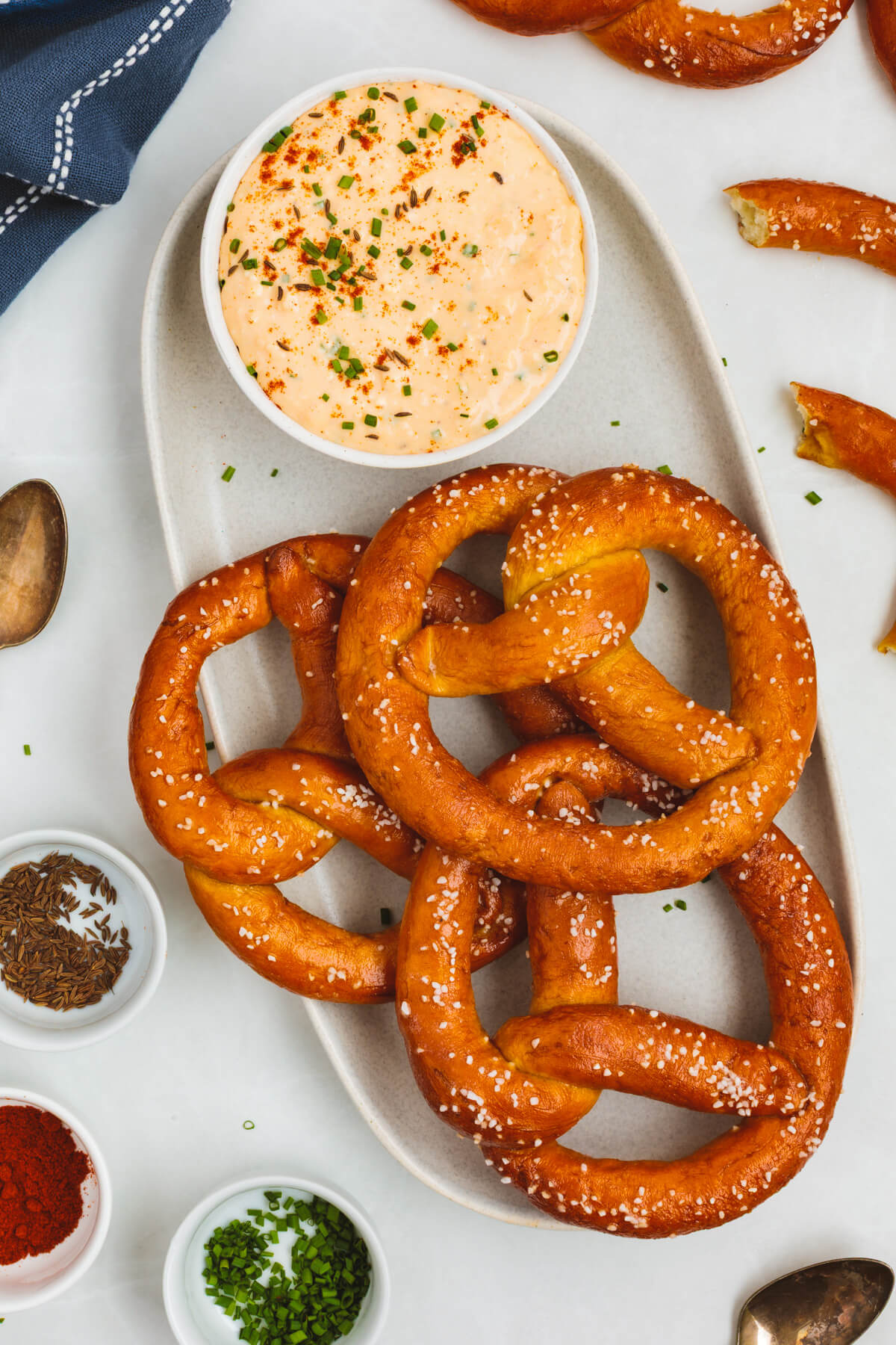 A white oval platter containing a bowl of Obatzda and three dark brown salty homemade pretzels.