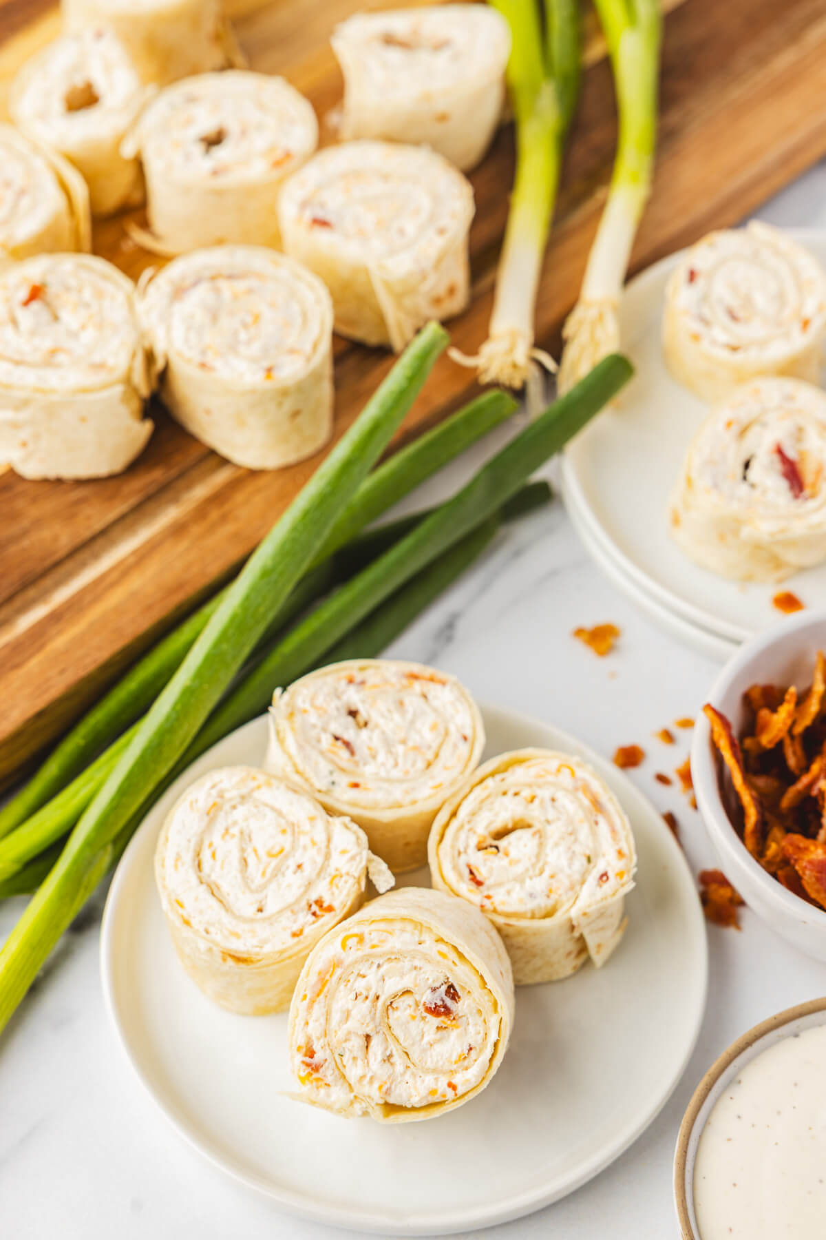 Two plates of tortilla pinwheels filled with cream cheese mixture containing bacon, cheddar cheese, and shredded chicken.