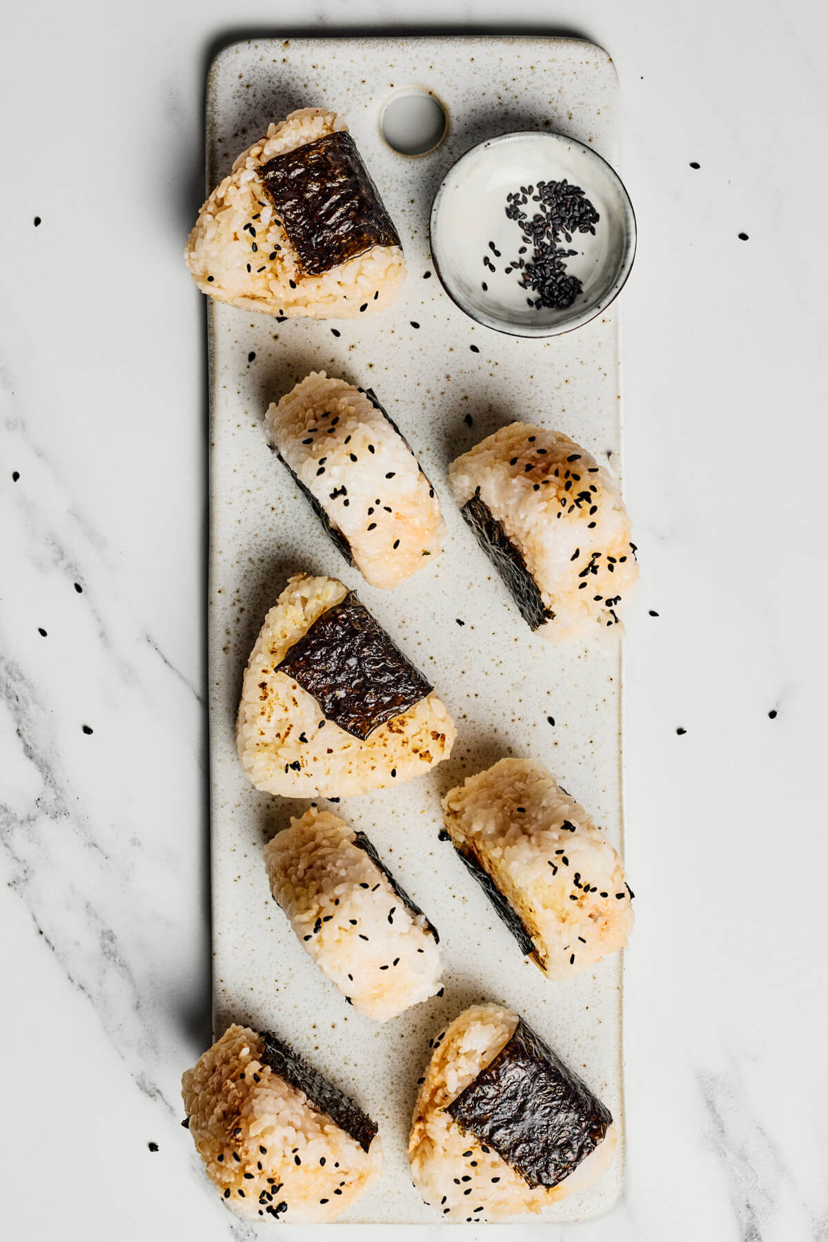 A tray of seasoned Japanese Onigiri wrapped in nori and garnished with black sesame seeds.