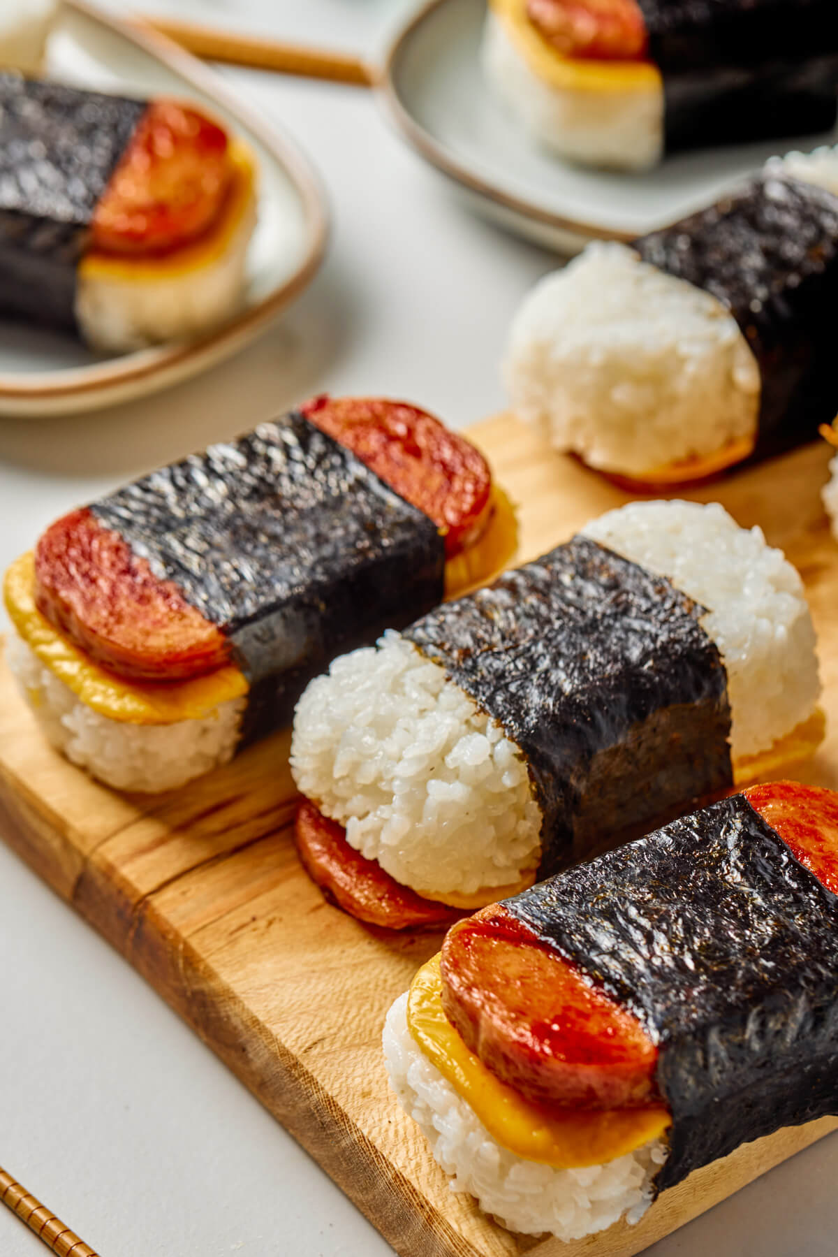 Three Spam and Egg Musubi wrapped in nori strips on a wooden serving board. 
