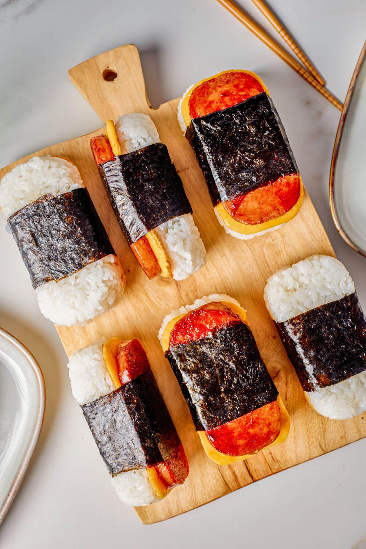 Six Spam and Egg Musubi wrapped in nori strips on a wooden serving board.