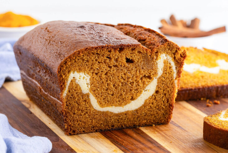 A loaf of orange tinted Cream Cheese Pumpkin Bread sliced open to show the ribbon of cream cheese baked into the center.