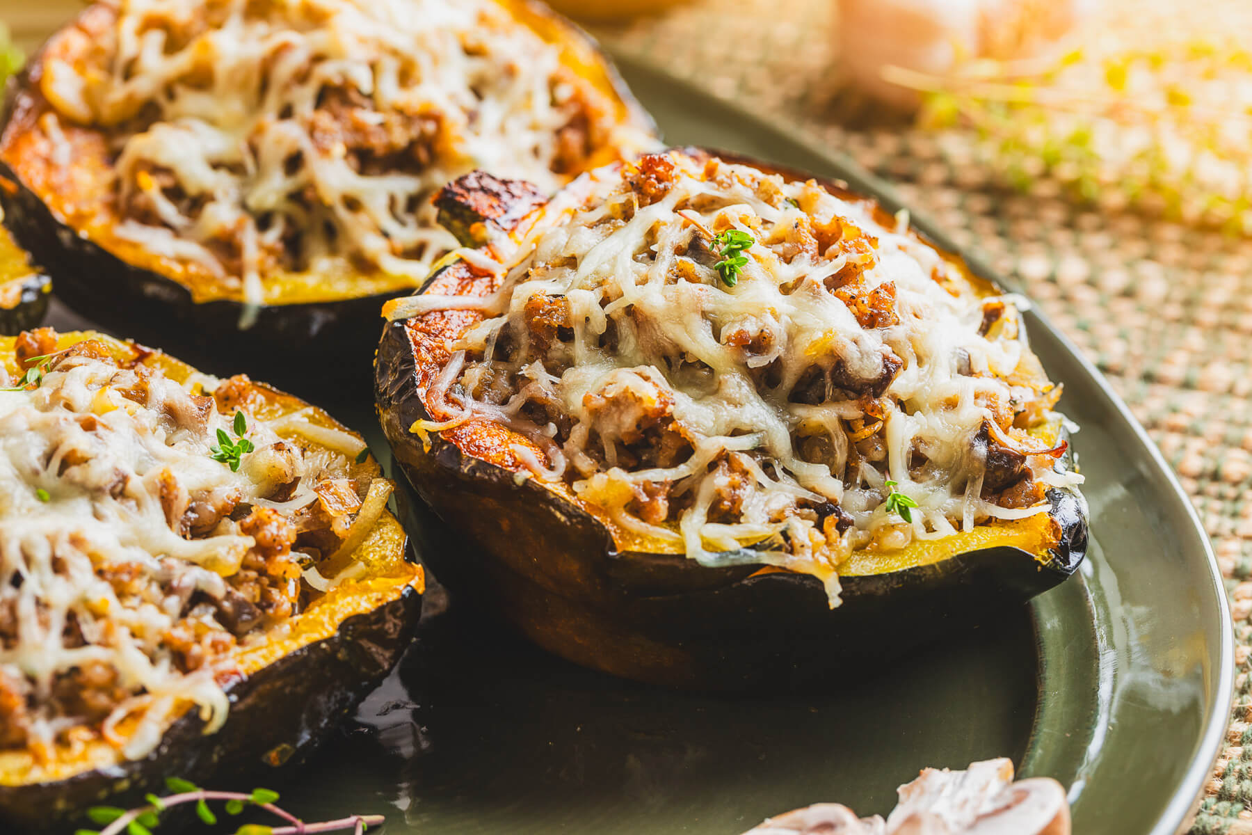 Three halves of roasted acorn squash stuffed with sausage filling and topped with melted mozzarella cheese on a green platter.