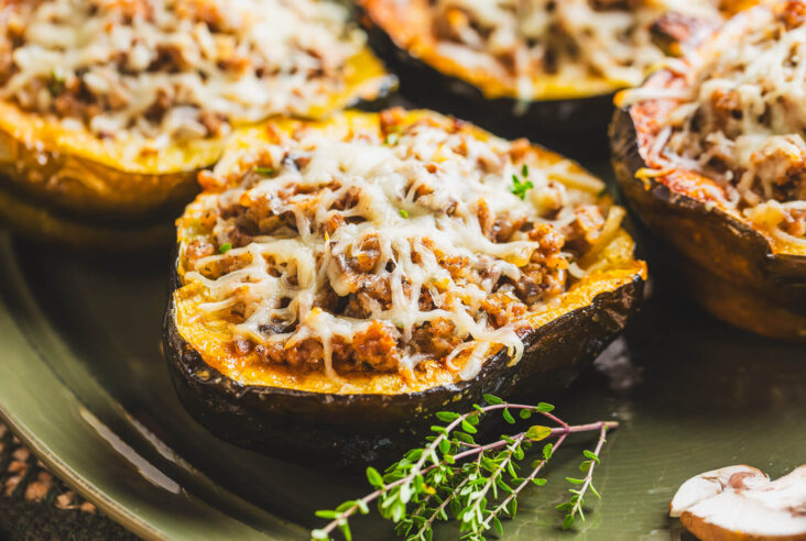 Four halves of roasted acorn squash stuffed with sausage filling and topped with melted mozzarella cheese on a green platter.