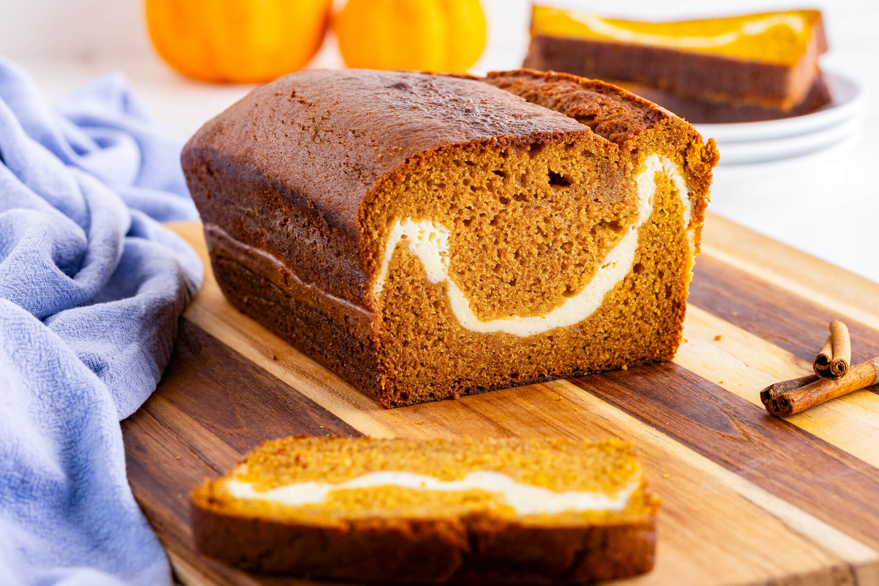 A cream cheese pumpking loaf on a wooden cutting board with one slice sliced off showing the cream cheese swirl.