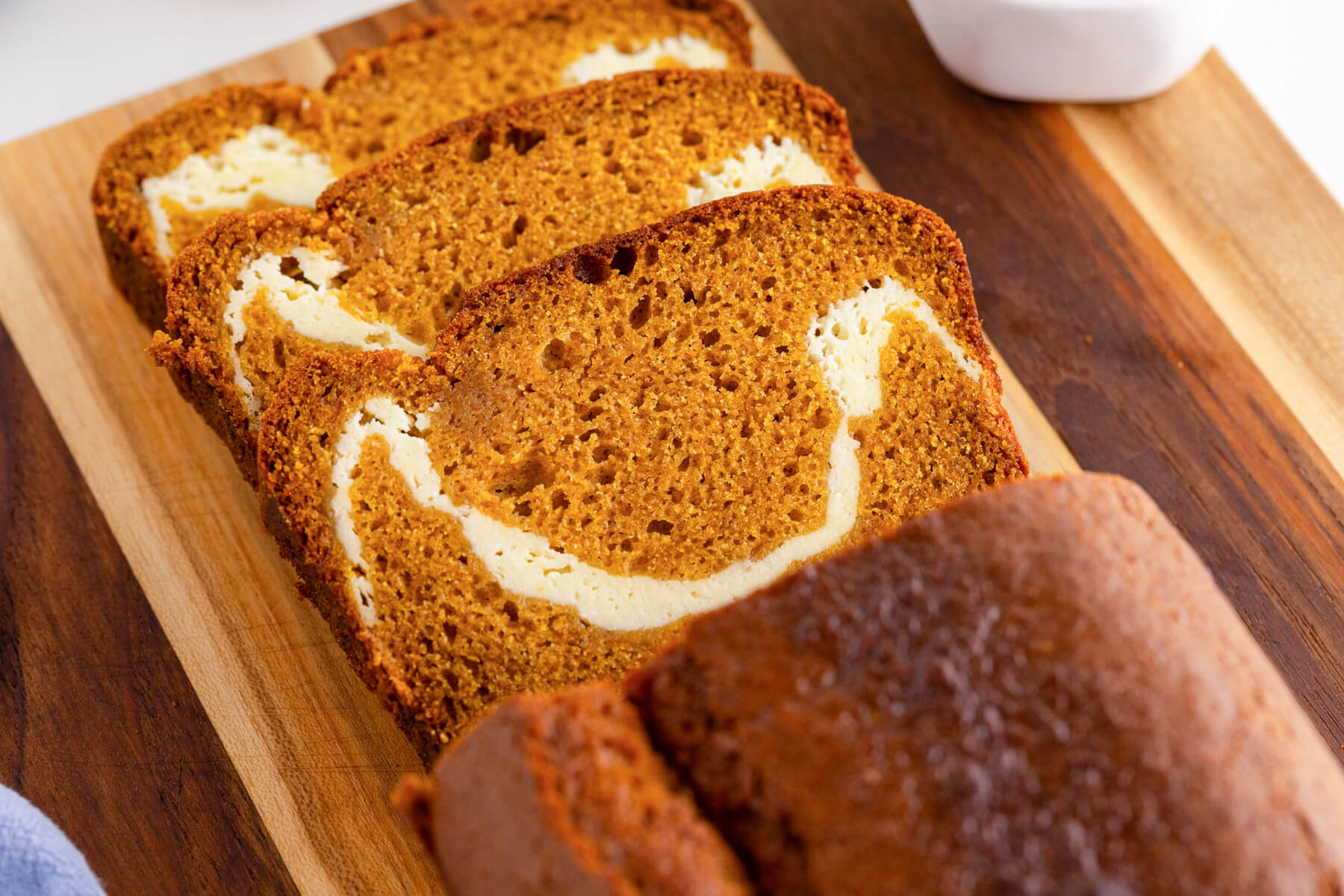 A cream cheese pumpking loaf on a wooden cutting board with three slices sliced off showing the cream cheese swirl.