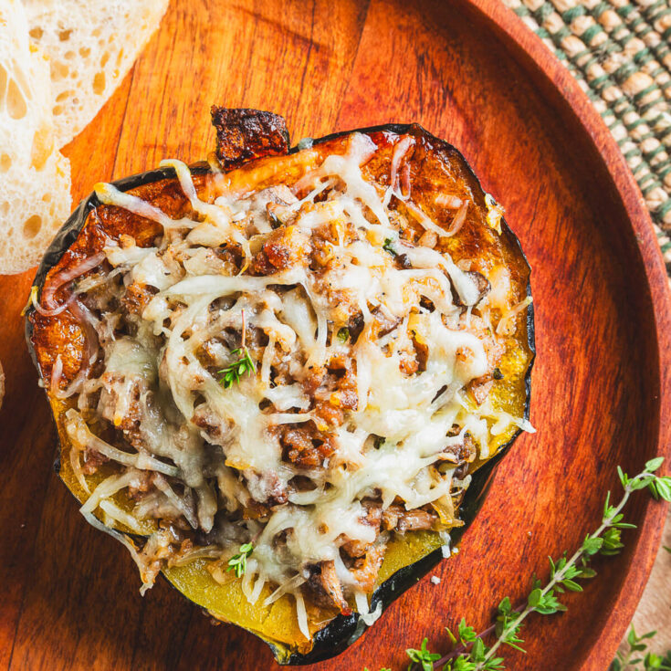One half of a roasted acorn squash stuffed with sausage filling and topped with melted mozzarella cheese on a wooden plate.