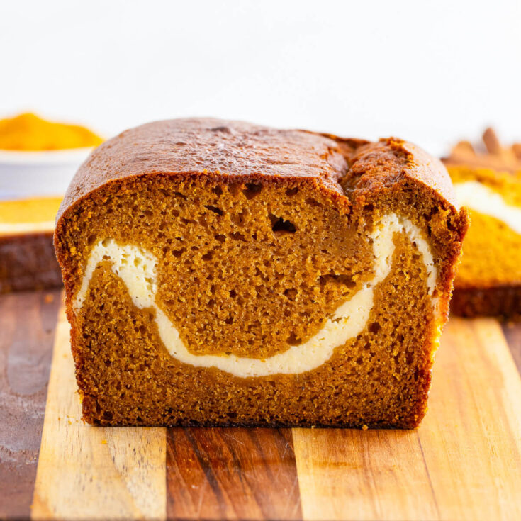A loaf of of sliced orange tinted Cream Cheese Pumpkin bread with a white ribbon of cream cheese baked into the center.